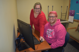 bbin信誉网站的一名学生坐在办公桌前，而残疾人服务中心的工作人员在使用电脑