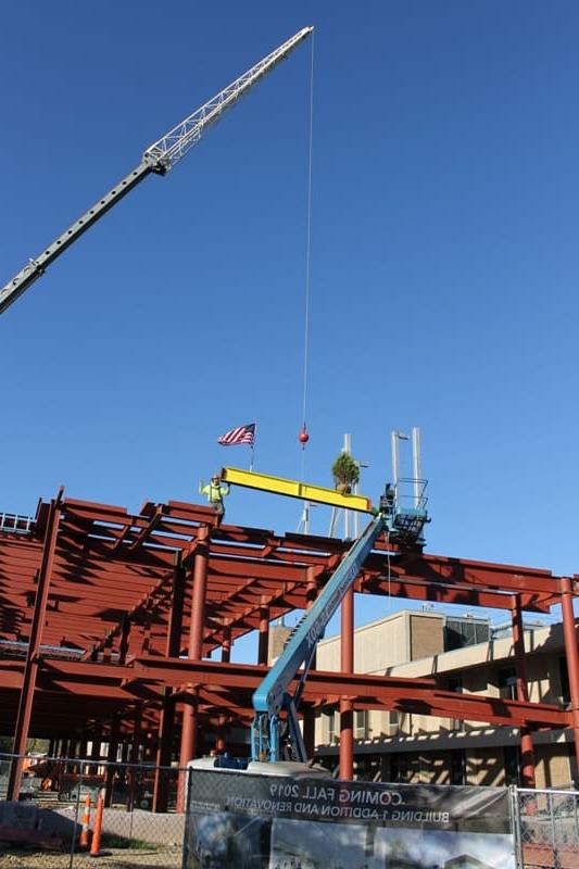 鹤落黄梁与常绿 & 美国国旗落在新的两层楼的红色钢框架顶部的工人