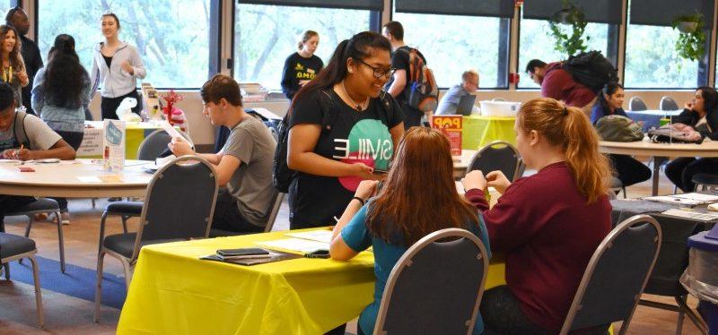 在组织博览会上，一名学生与坐在桌子旁的两名学生交谈