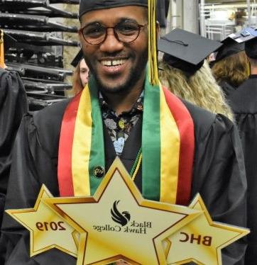 Graduate wearing black cap and gown holding BHC 2019 sign