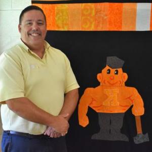 Kewanee High School teacher standing in front of a quilt featuring the school's mascot, 一个锅炉制造厂
