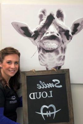 woman holding a Smile LOUD sign with art of a giraffe wearing braces behind her