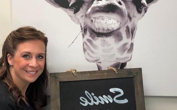 woman holding a sign that reads smile loud with an image of a giraffe wearing braces behind her