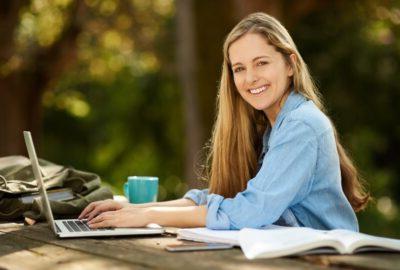 young woman sitting at a table outdoors with a laptop and school supplies